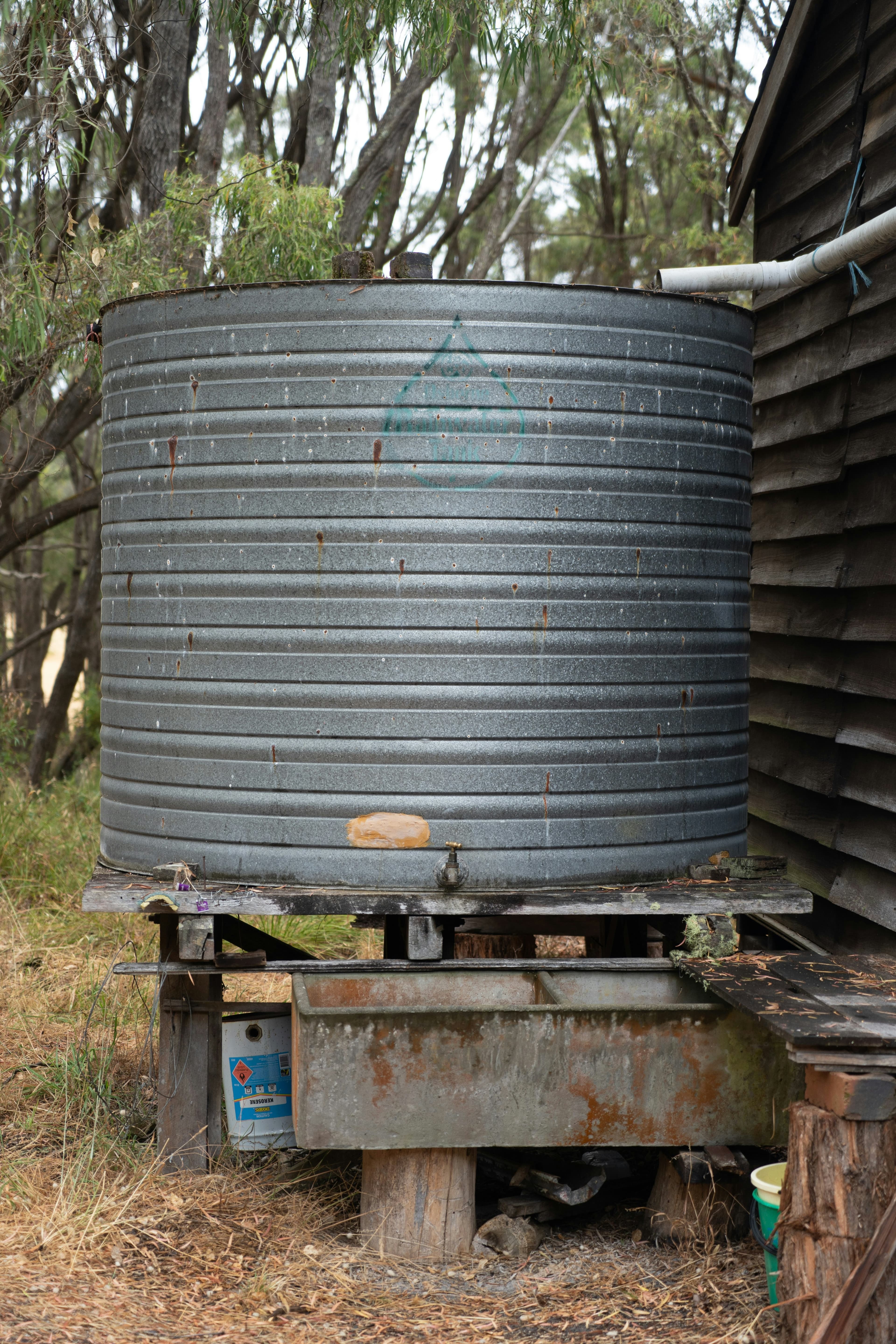 Round metal rainwater tank beside a garden, same cylinder model as a rain barrel
